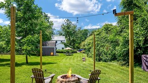 Un patio trasero con un pozo de fuego, dos sillas Adirondack, un pérgola de madera y una casa al fondo.