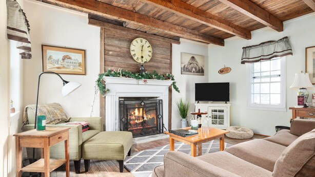 Una sala de estar acogedora con chimenea, vigas de madera, un reloj y un televisor.