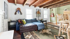 Una sala de estar acogedora con un sofá azul, un reposapiés de cuero marrón y una mesa de comedor de madera con sillas.