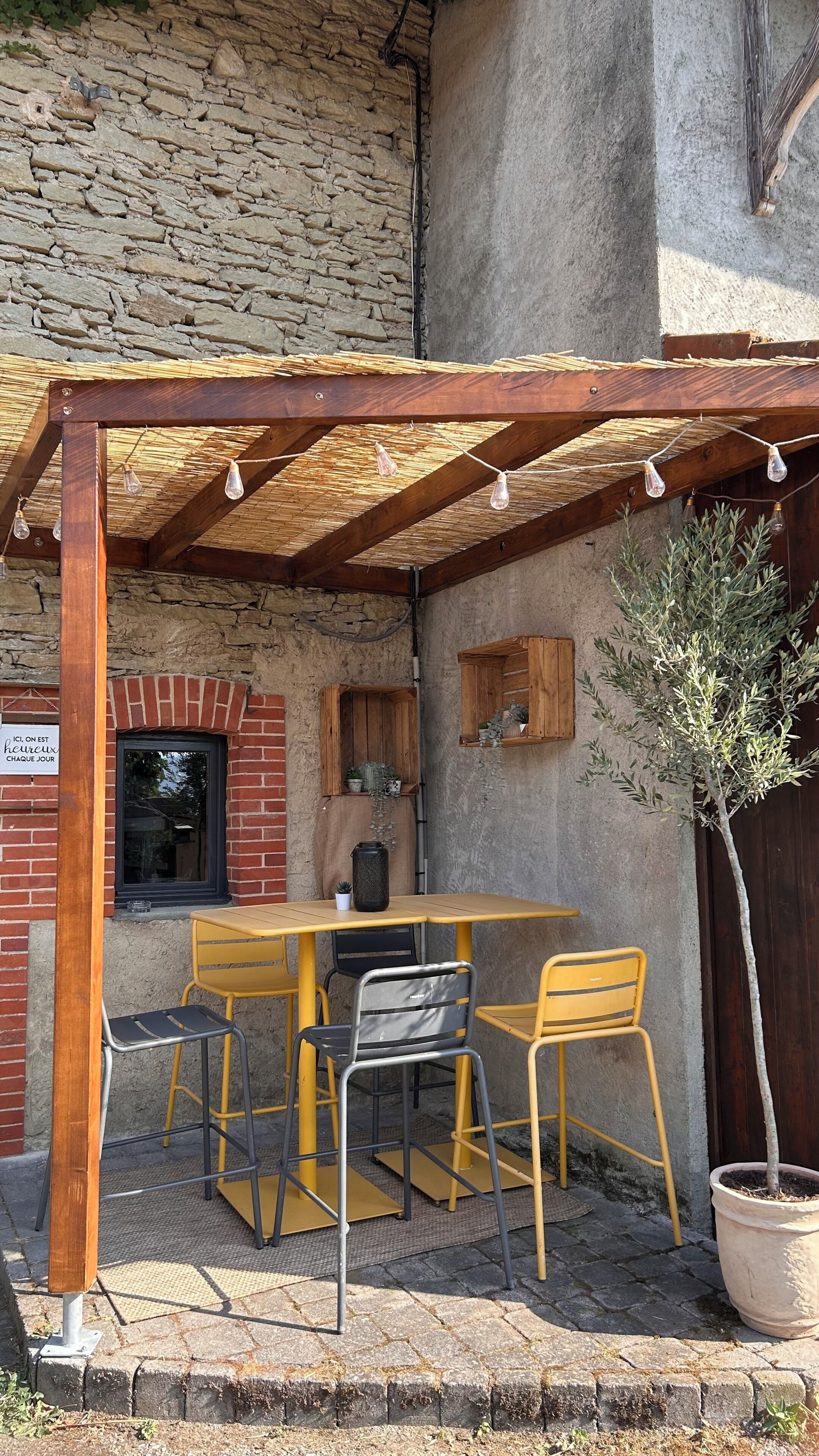 Un patio al aire libre con una pérgola de madera, una mesa, sillas y una planta en maceta.