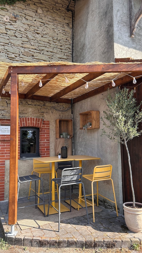 An outdoor patio with a wooden pergola, a table, chairs, and a potted plant.