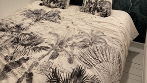 A bed with a tropical leaf pattern bedspread, two matching pillows, and a woven light fixture above.