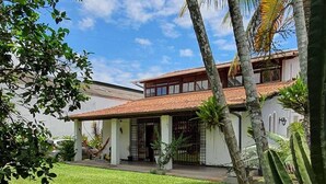 A house with a tiled roof, a covered porch, and a well-maintained lawn. - chacaradaspalmeiras512 -Inoan-Marica-RJ-lots of greenery, swimming pool, sauna, (marica)
