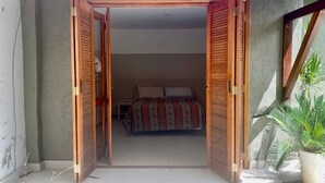 An open wooden door leading to a bedroom with a bed and a nightstand. - chacaradaspalmeiras512 -Inoan-Marica-RJ-lots of greenery, swimming pool, sauna, (marica)