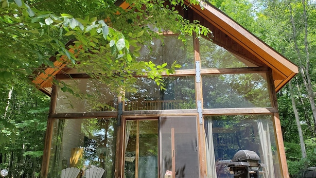 Una cabaña de madera con ventanas amplias, una terraza y una parrilla.