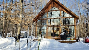 Una cabaña de madera con ventanas amplias, rodeada de nieve y árboles.
