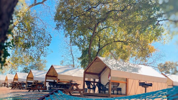 A hammock with a view of a campsite including tents and tables. - Son's Blue River Camp - Glamping Cabin #1 (Kingsbury)
