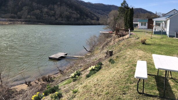 Une vue sur la rivière, avec un quai, des tables de pique-nique et des maisons en arrière-plan.