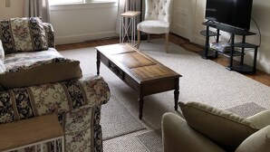 Un salon comprenant un canapé, un fauteuil, une table basse et un téléviseur posé sur un meuble.