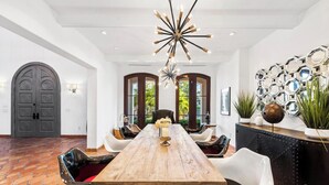Un comedor amplio con una larga mesa de madera, sillas blancas y un moderno candelabro.