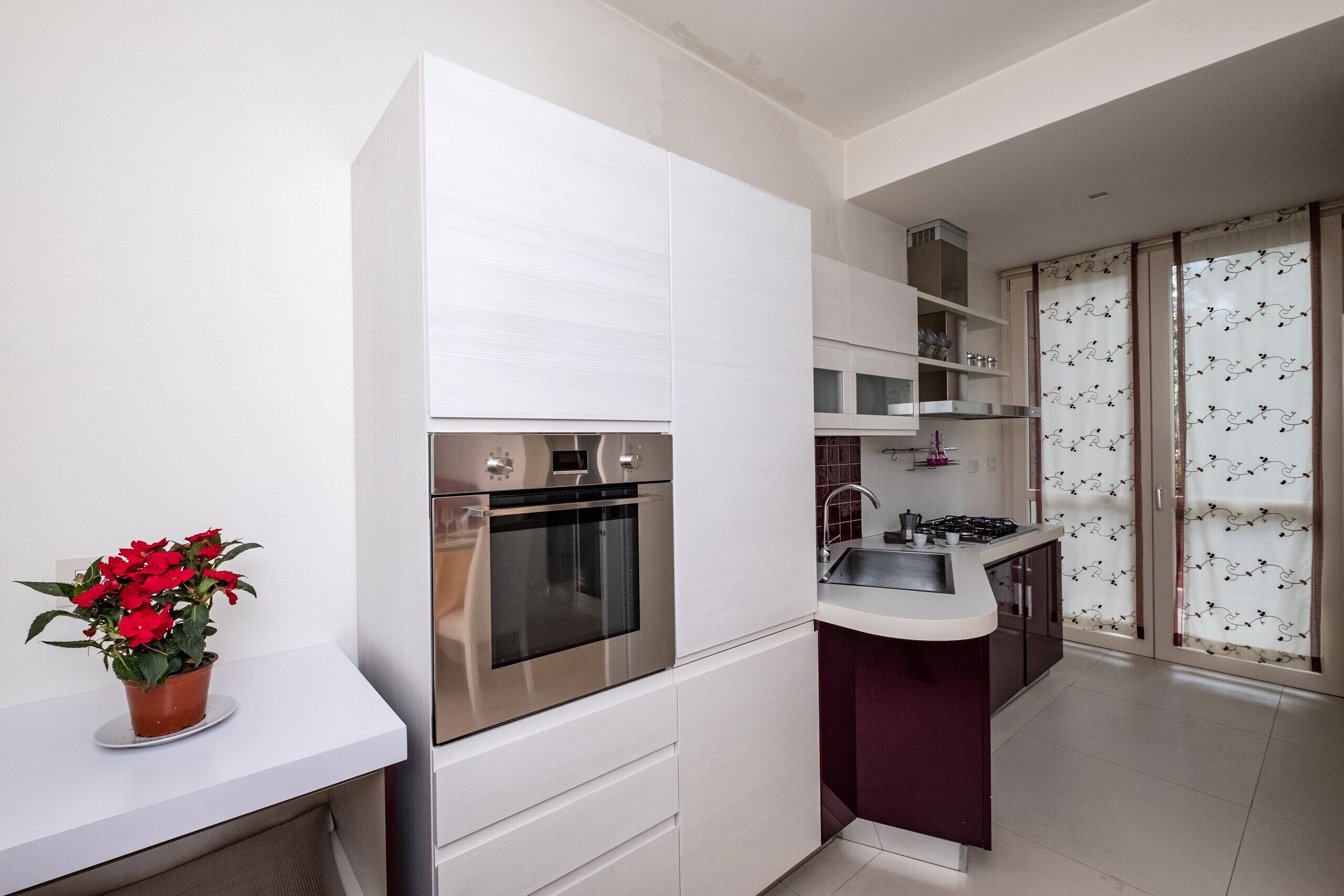 A modern kitchen with white cabinetry, a stainless steel oven, and a small island with a sink.
