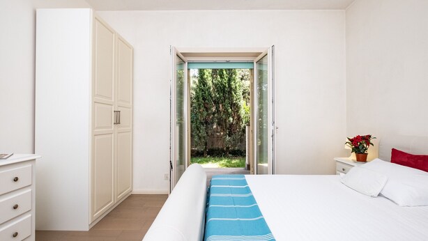 Ein Schlafzimmer mit Bett, Nachttisch, Kommode und einer Schiebetür, die in einen Garten führt.