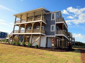 A multi-story residential building with a balcony on each floor, a covered porch, and a landscaped yard. - Ocean & Sound Views, 4BR Coastal Retreat, Fenced Dog Run, Near Camp Lejeune (North Topsail Beach)
