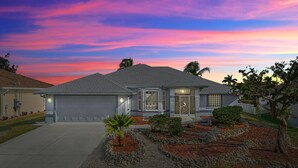 Une maison de plain-pied avec un garage, un porche à l’avant et un jardin aménagé avec un palmier et des arbustes.