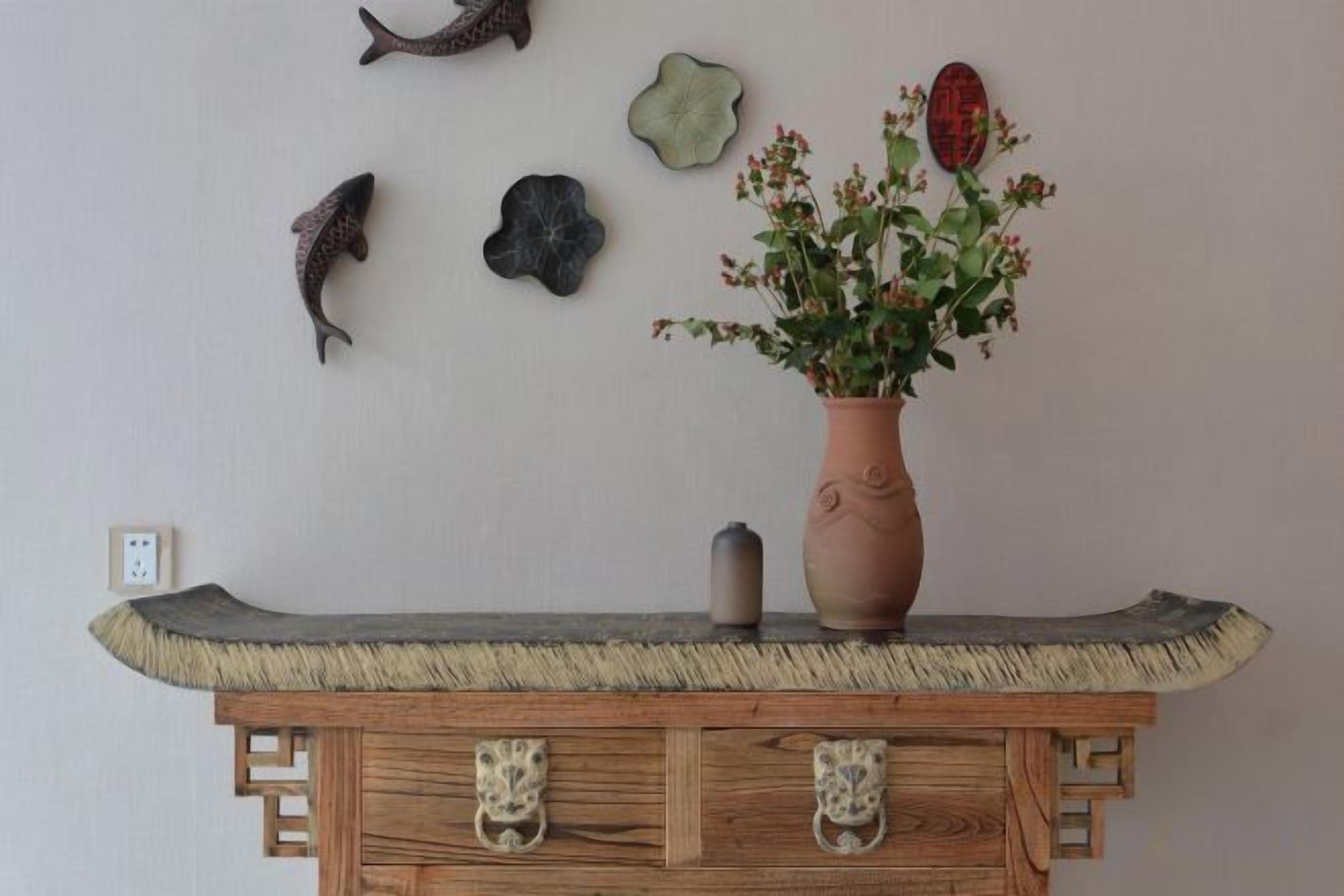 A wooden console table with a vase of flowers, a small decorative item, and wall decorations including fish and a flower.