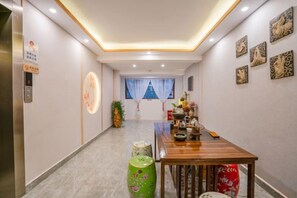 Un pasillo con una mesa de madera, un jarrón verde y un jarrón blanco. Hay un cartel en la pared y una ventana con cortinas azules.