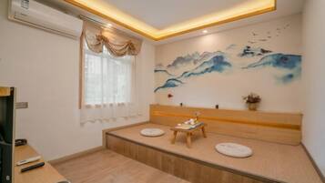 Quarto com um banco de madeira, ar condicionado fixado na parede, janela com cortinas e um quadro de montanhas.
