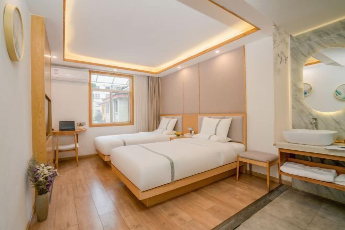 A modern hotel room with two beds, a desk, a vanity with a mirror, and a window.