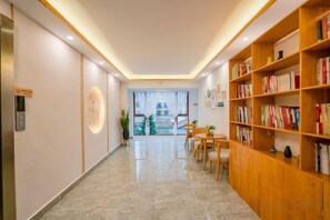 Un hall d’hôtel comprenant un comptoir d’accueil, une horloge, une bibliothèque et une vue sur un bâtiment situé à l’extérieur.