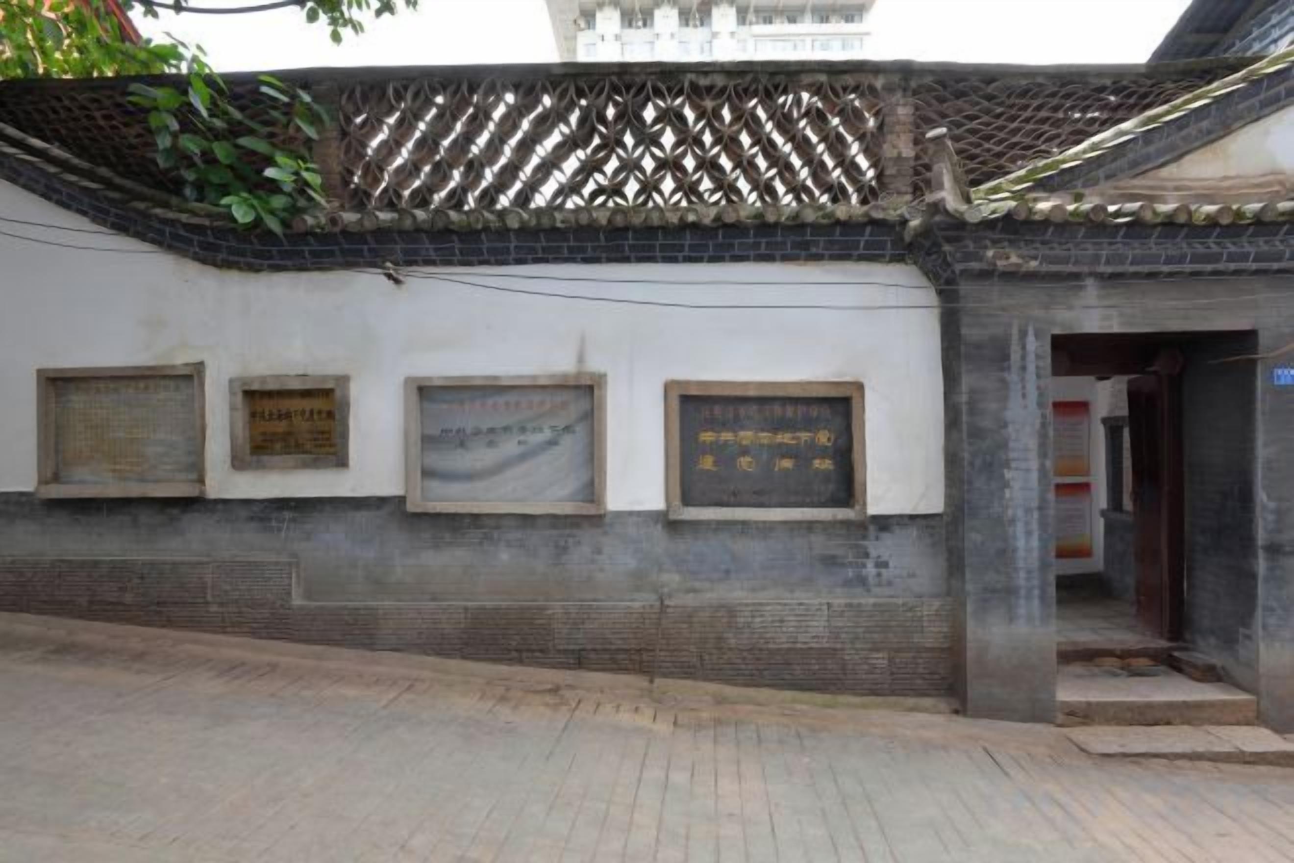 A building with a tiled roof and a brick wall. There are three plaques on the wall.