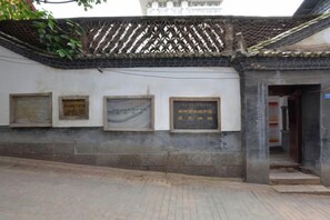 Un bâtiment avec un toit recouvert de tuiles et un mur en briques. On peut y voir trois plaques fixées au mur.