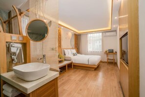Un dormitorio moderno con una cama grande, una mesita de noche, un espejo redondo, un lavamanos empotrado y un escritorio pequeño.