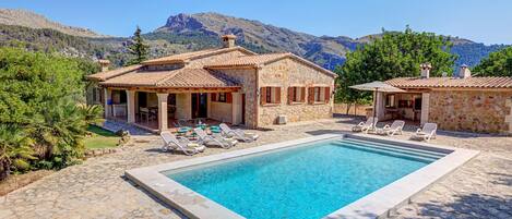 A pool area with lounge chairs and a stone building with a tiled roof.