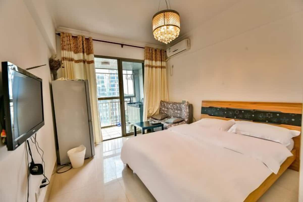 Habitació d'hotel amb llit, televisió, taula petita, cadira i balcó amb cortines.