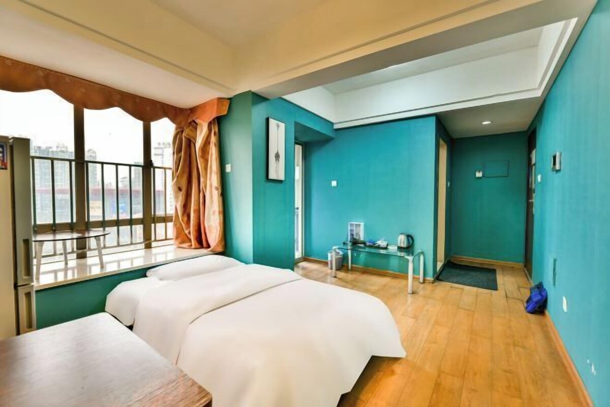 Habitación de hotel con cama, una mesita, ventana con cortinas y vista a la ciudad.