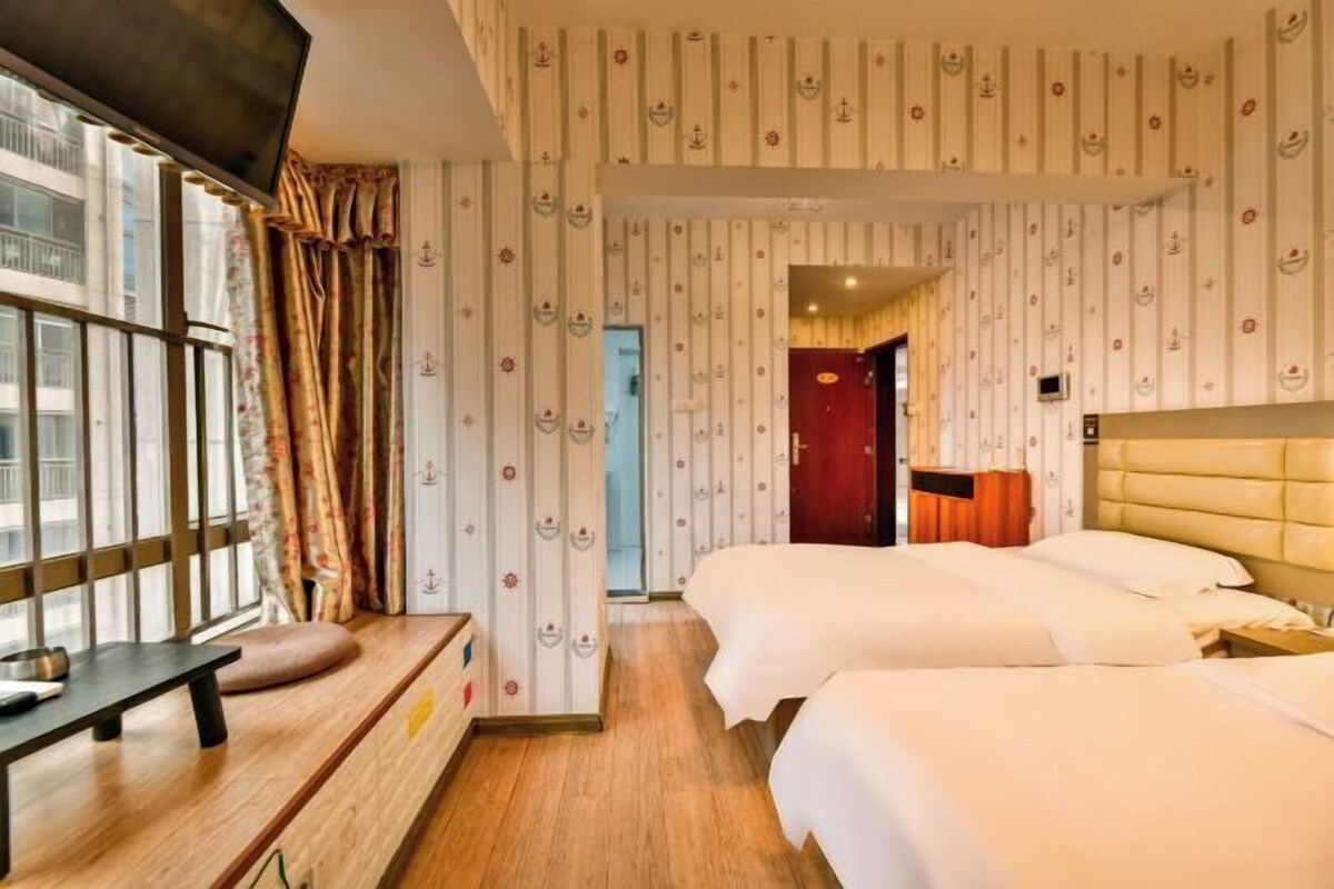 Habitación de hotel con dos camas, un escritorio, un televisor y una ventana con cortinas.