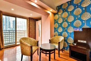 Una habitación con dos sillones estampados, una mesita de cristal, una chimenea y un ventanal con cortinas.