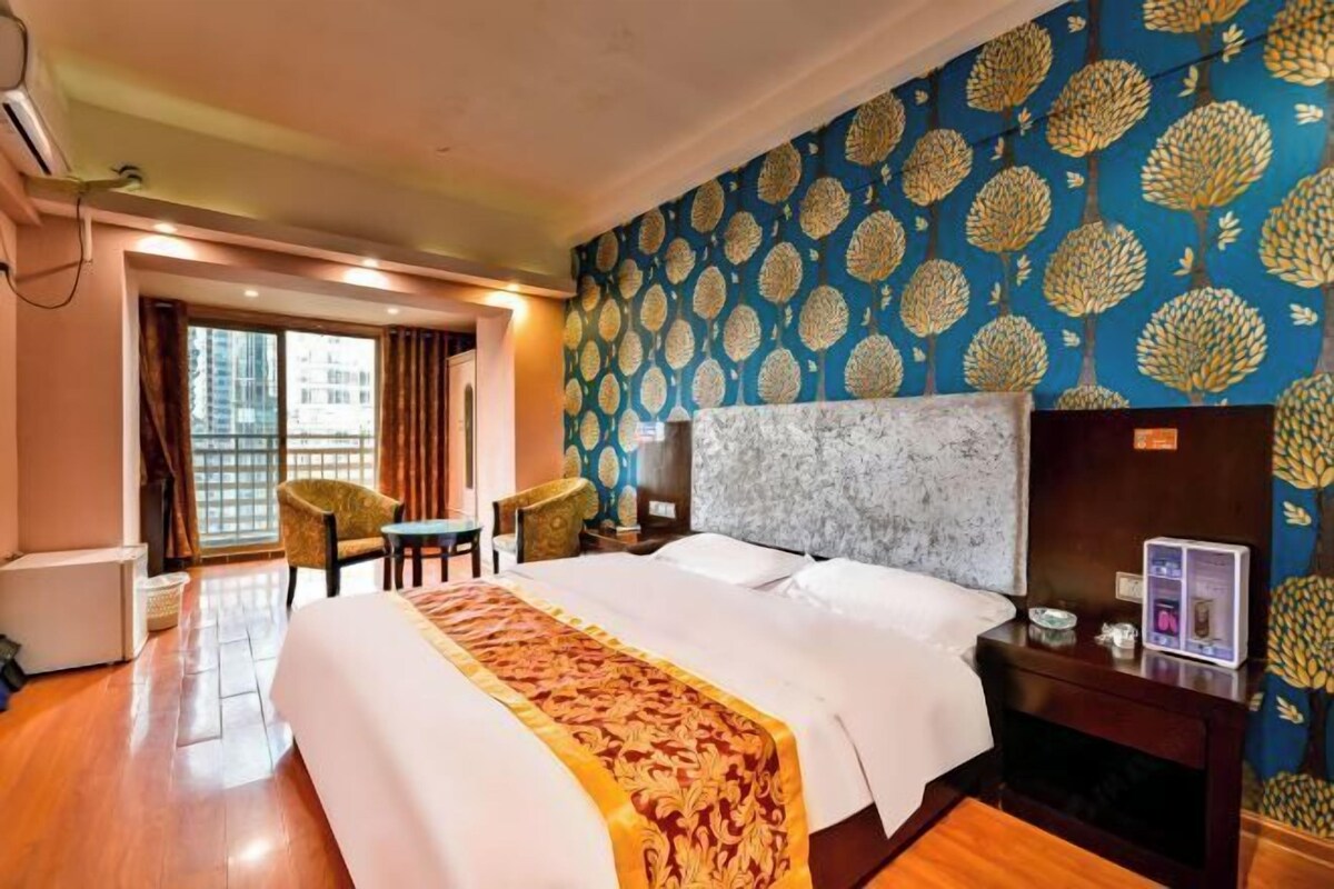 Habitación de hotel con una cama grande, un escritorio, una silla y vistas a la ciudad por la ventana.
