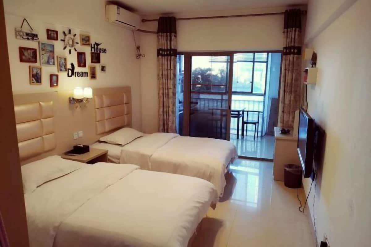 Habitació d'hotel amb dos llits, televisió, un balcó amb taula i cadires, i una paret amb quadres i la inscripció 'Dream House'.