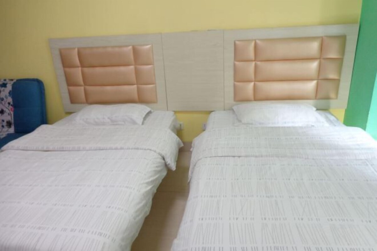 Dos camas individuales con cabeceros, una silla azul y una pared amarilla.
