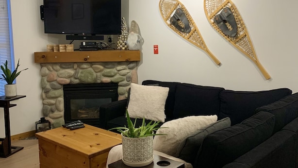 Moderni olohuone, jossa on takka, seinälle asennettu televisio ja musta sohva.