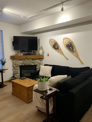 A modern living room with a fireplace, a television mounted on the wall, and a black sofa.