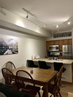 A modern kitchen with wooden cabinets, stainless steel appliances, and a dining area with a wooden table and chairs.