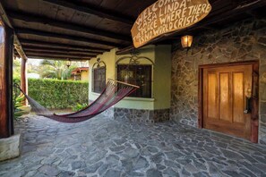 A stone-walled building with a hammock, a wooden door, and a sign.