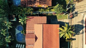 Vista aérea de una propiedad residencial con piscina, un patio con sillones de descanso y un jardín con palmeras.