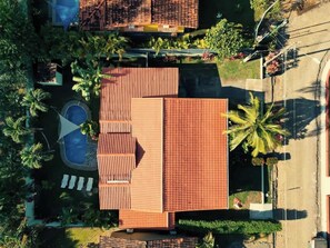 An aerial view of a residential property with a swimming pool, a patio with lounge chairs, and a garden with palm trees.