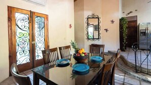 Un comedor con una mesa de vidrio, sillas, un frutero y un espejo en la pared.