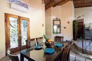 A dining area with a glass table, chairs, a fruit bowl, and a mirror on the wall.