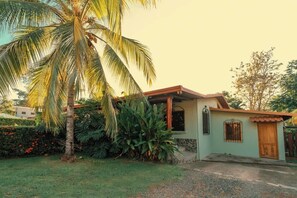 Una casa con porche, una palmera y un pequeño jardín.
