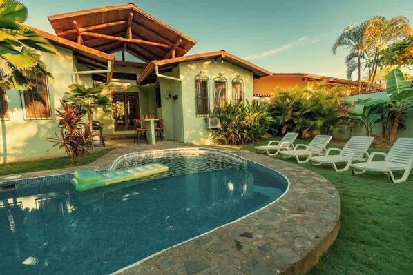 A poolside area with a stone pool, lounge chairs, and a covered patio.