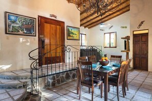 Un comedor con una mesa dispuesta para cuatro personas, rodeada de sillas, una escalera con barandilla y una puerta de madera.