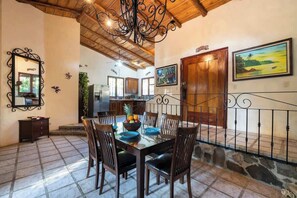 A dining area with a wooden table, chairs, a fruit bowl, and a decorative metal railing.