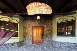 Entrada con muro de piedra, puerta de madera, una hamaca y un letrero que dice 'WELCOME TO CASA LINDA THE PLACE WHERE THERE IS NO WORLD CRISIS'.