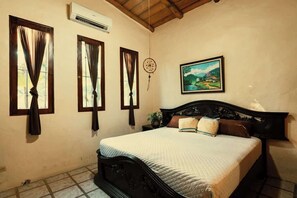 A bedroom with a bed, curtains, a wall-mounted air conditioner, a painting, and a wooden ceiling.