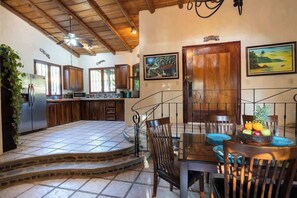 Una cocina amplia con armarios de madera, piso de baldosas de piedra y una zona de comedor con una mesa preparada para dos personas.