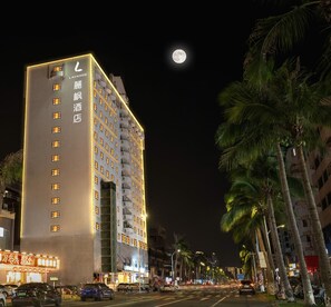A multi-story hotel with a prominent sign, a moon in the sky, and palm trees lining the street.